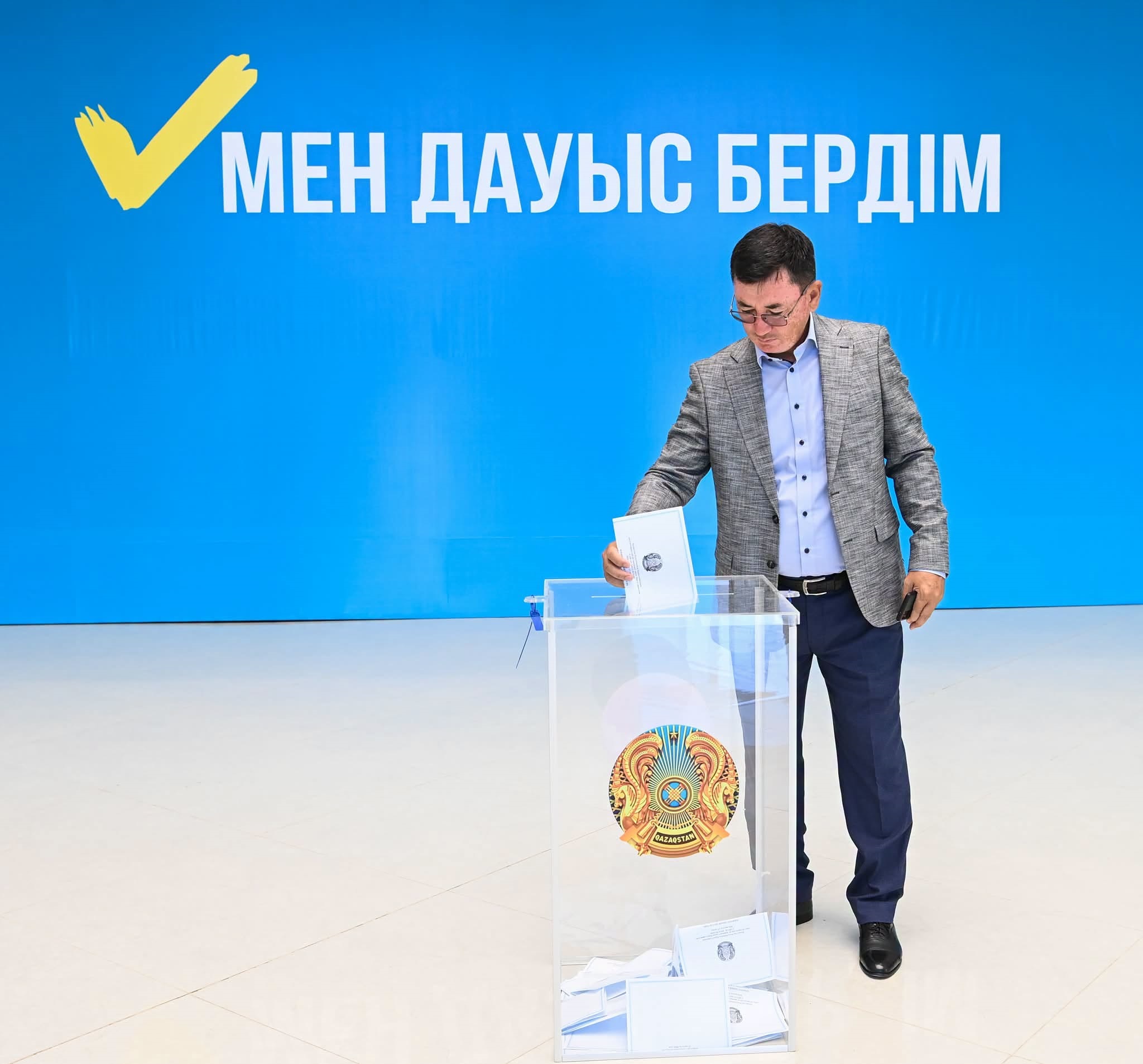 Ер адамның дауыс қорабына бюллетень салуы. Фонда «Мен дауыс бердім» деген жазу бар.