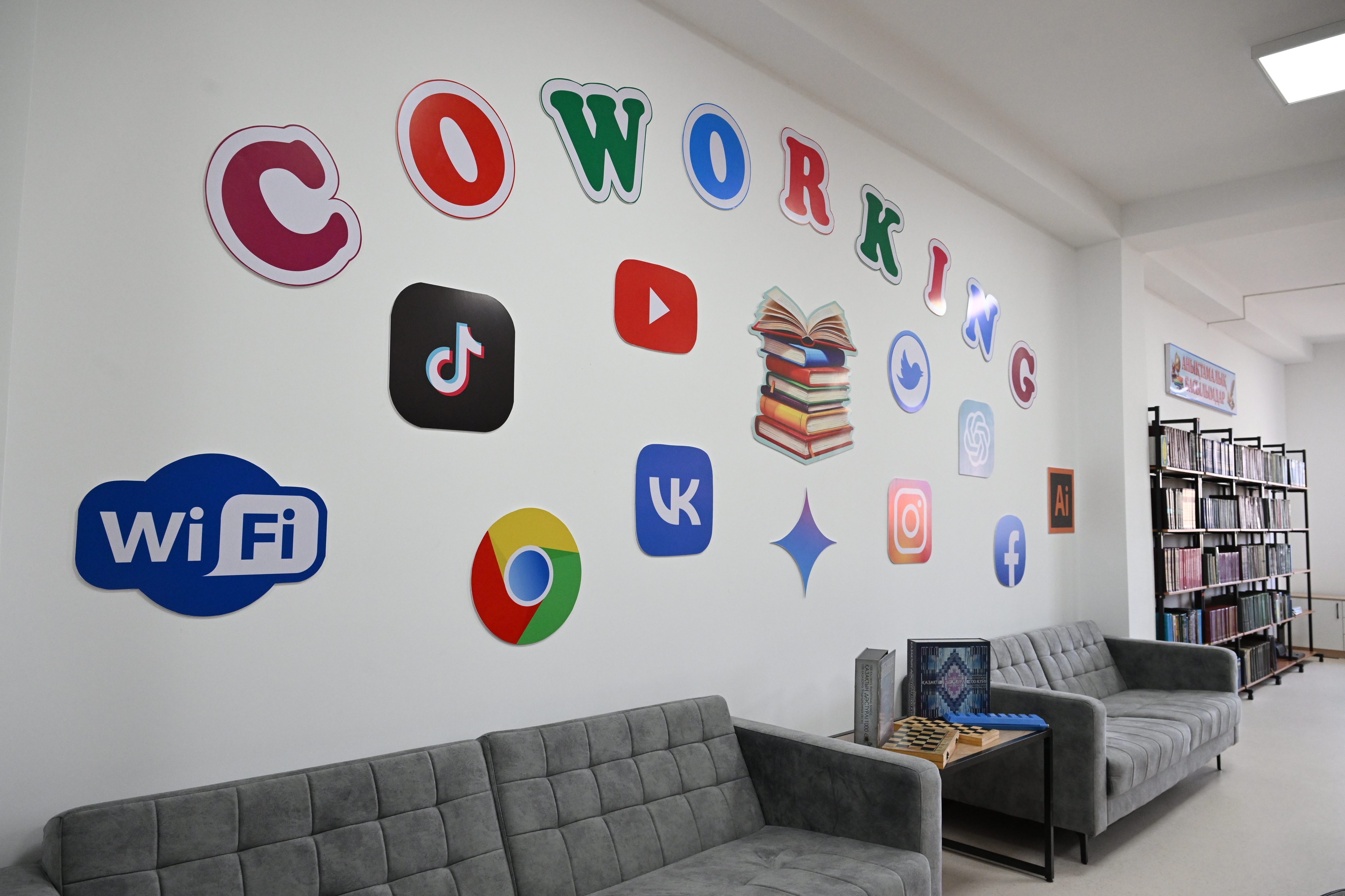 «COWORKING» жазуы және әлеуметтік желілер белгілері бейнеленген қабырғасы бар заманауи коворкинг кеңістігі.
