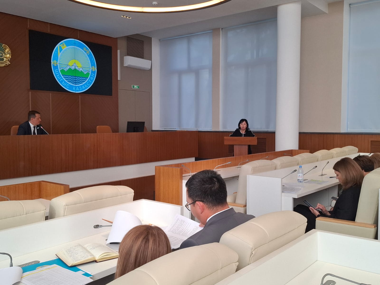 Суретте депутаттар алдында сессияның күн тәртібіндегі мәселе бойынша Шығыс Қазақстан облысы ішкі саясат басқармасы басшысының орынбасары А. Т. Жұмабаева баяндама жасайды.