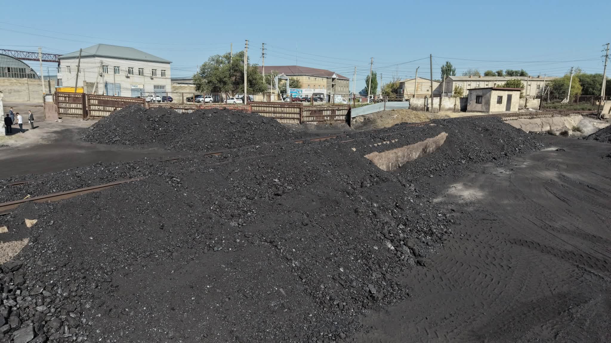 Теміржол рельстерінің жанындағы көмір үйінділері және артқы фондағы ғимараттар.