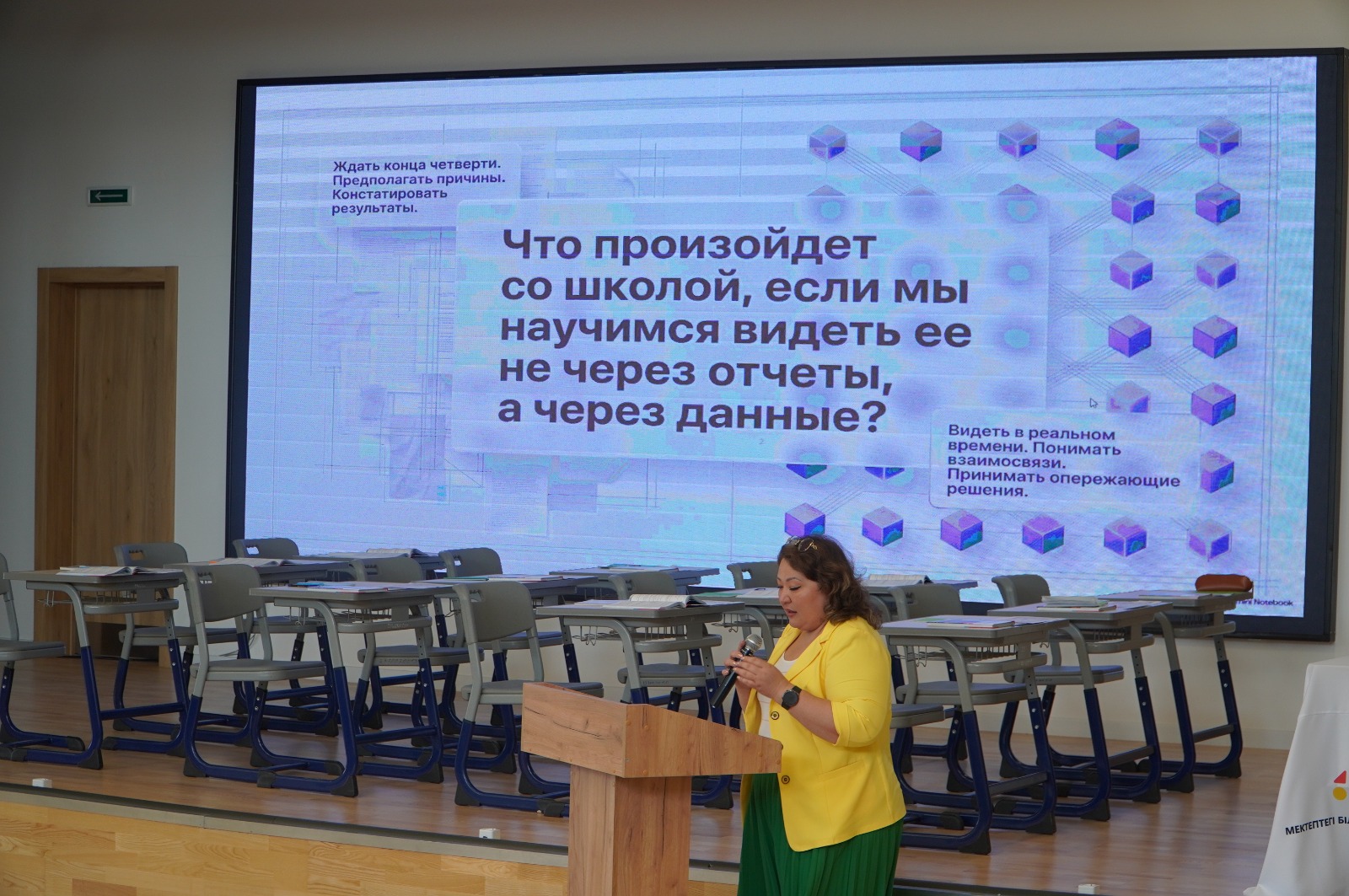 Сары пиджак киген әйел экрандағы презентация бойынша баяндама жасап тұр.
