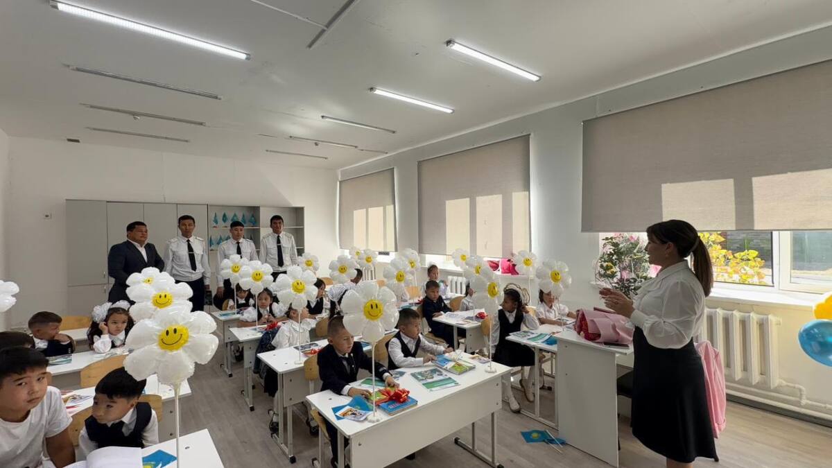 Сыныпта мұғалім мен оқушылардың сабағы. Сынып гүл пішінді әшекейлермен безендірілген.