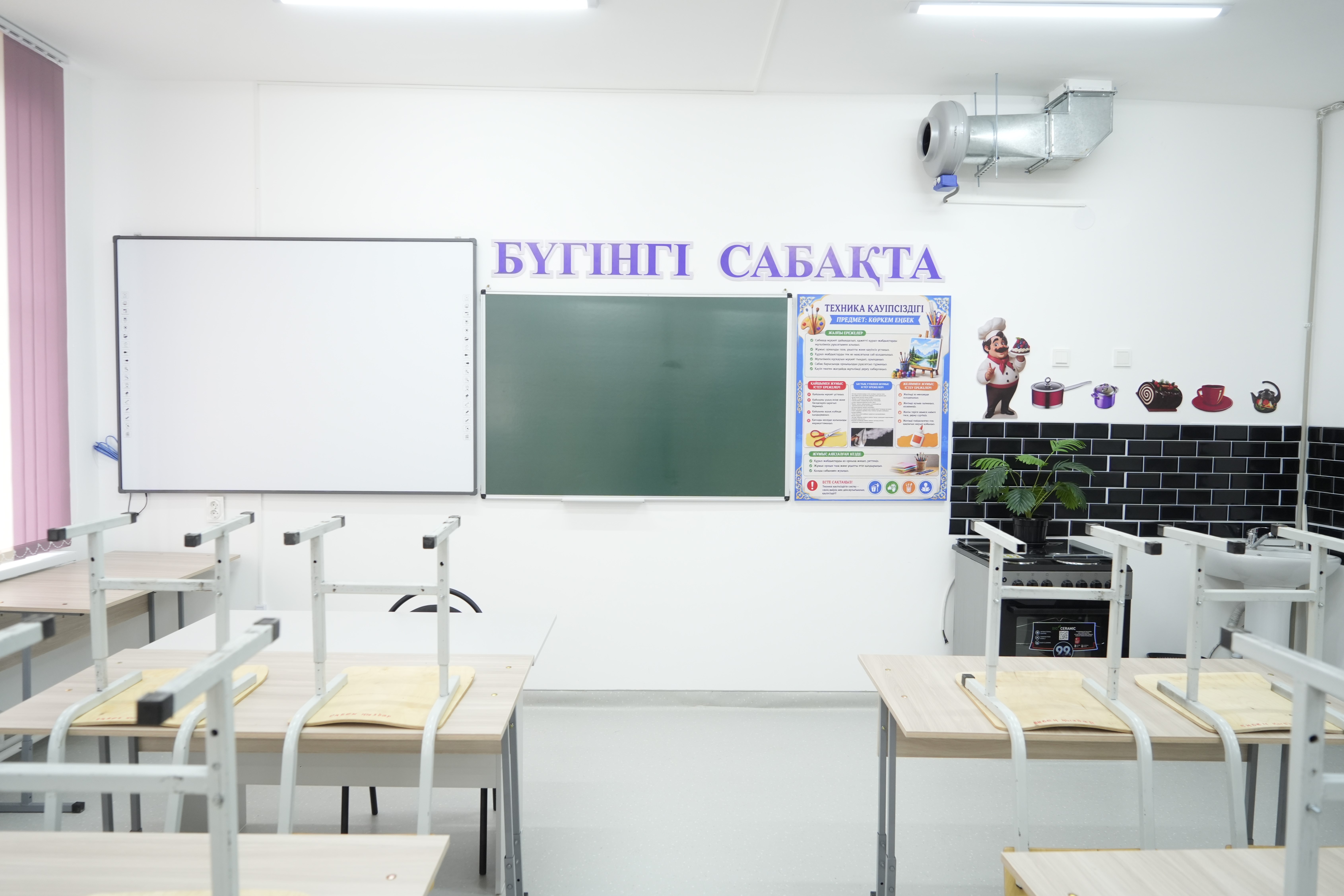 Светлый учебный класс кулинарии с досками, столами для учеников и зоной приготовления пищи.