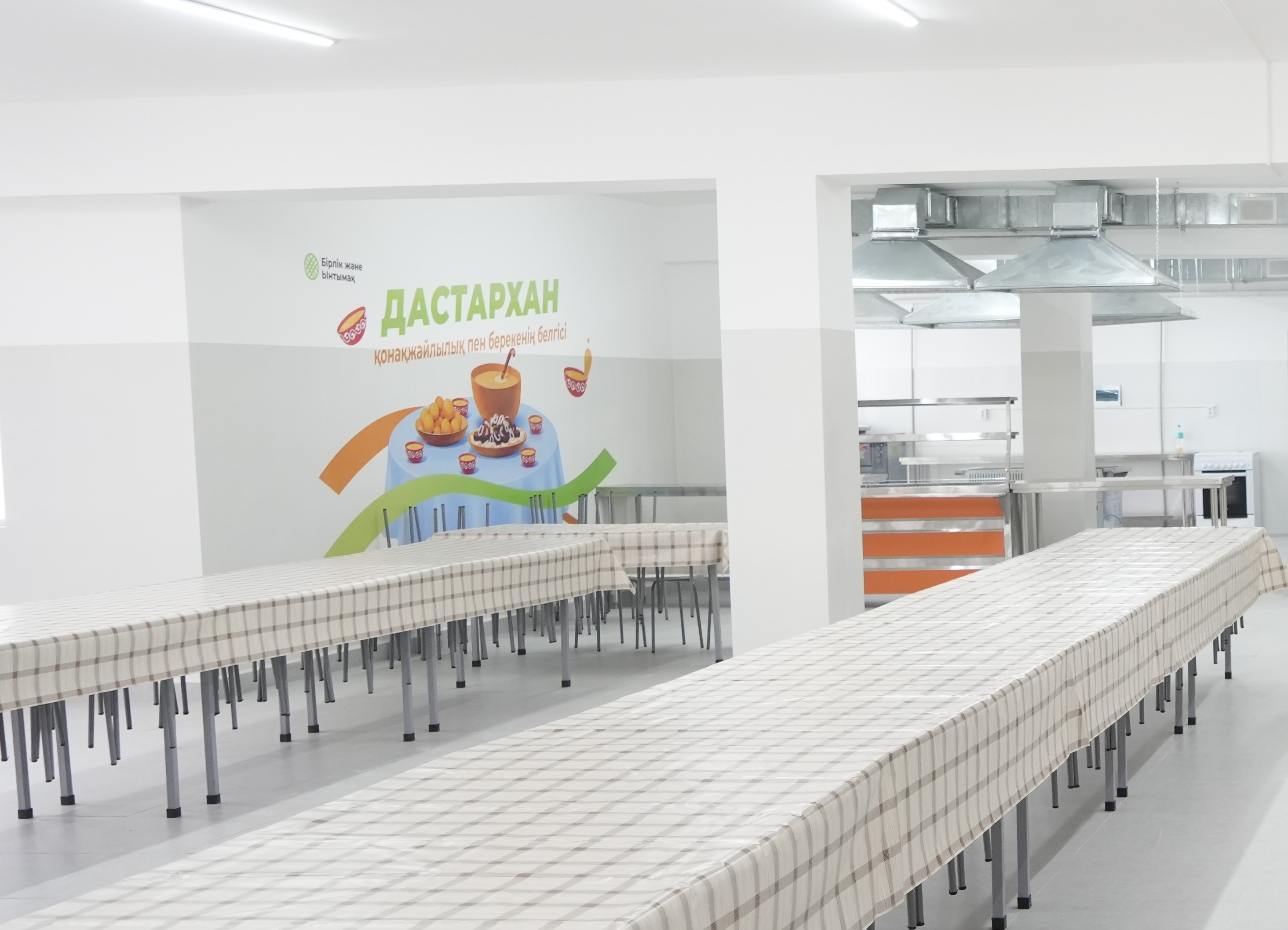 Столовая с длинными столами в клетчатых скатертях и ярким рекламным плакатом «Дастархан» на стене.