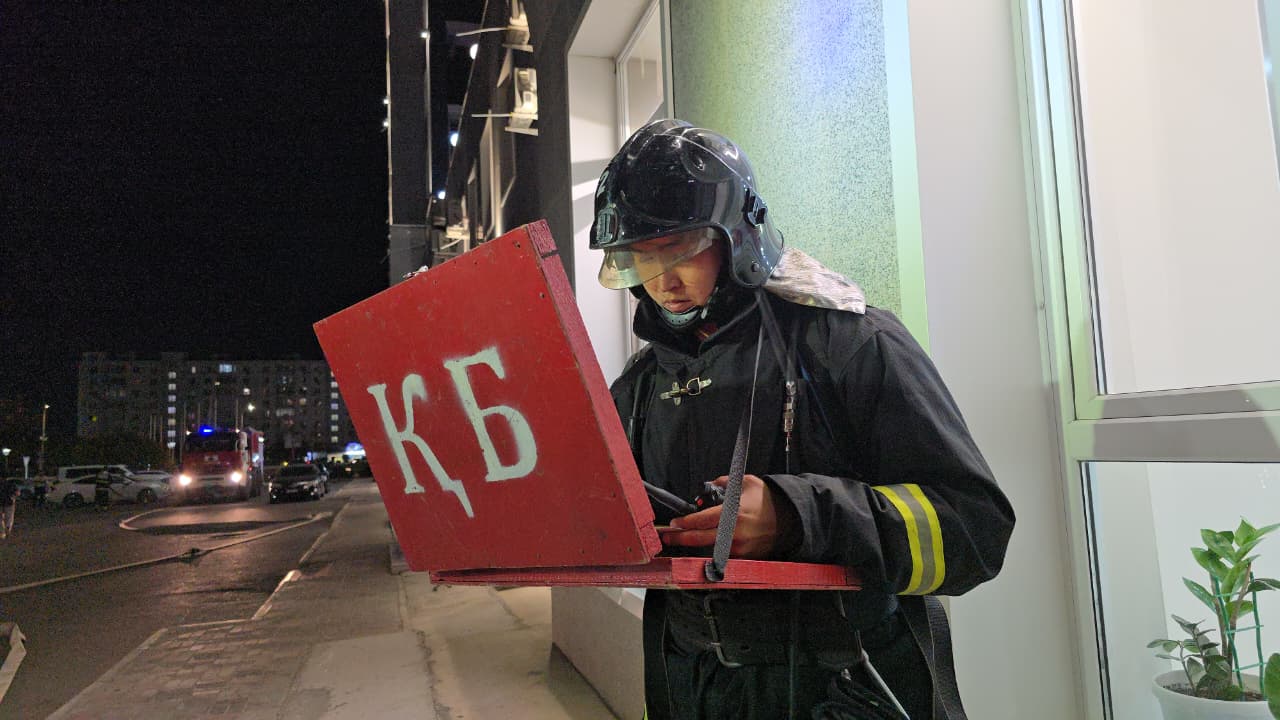 Түнгі уақытта «КБ» белгісі бар қызыл тақтаны ұстап тұрған өрт сөндіруші.