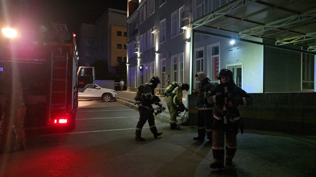 Пожарные в полной экипировке и пожарная машина у здания в ночное время.