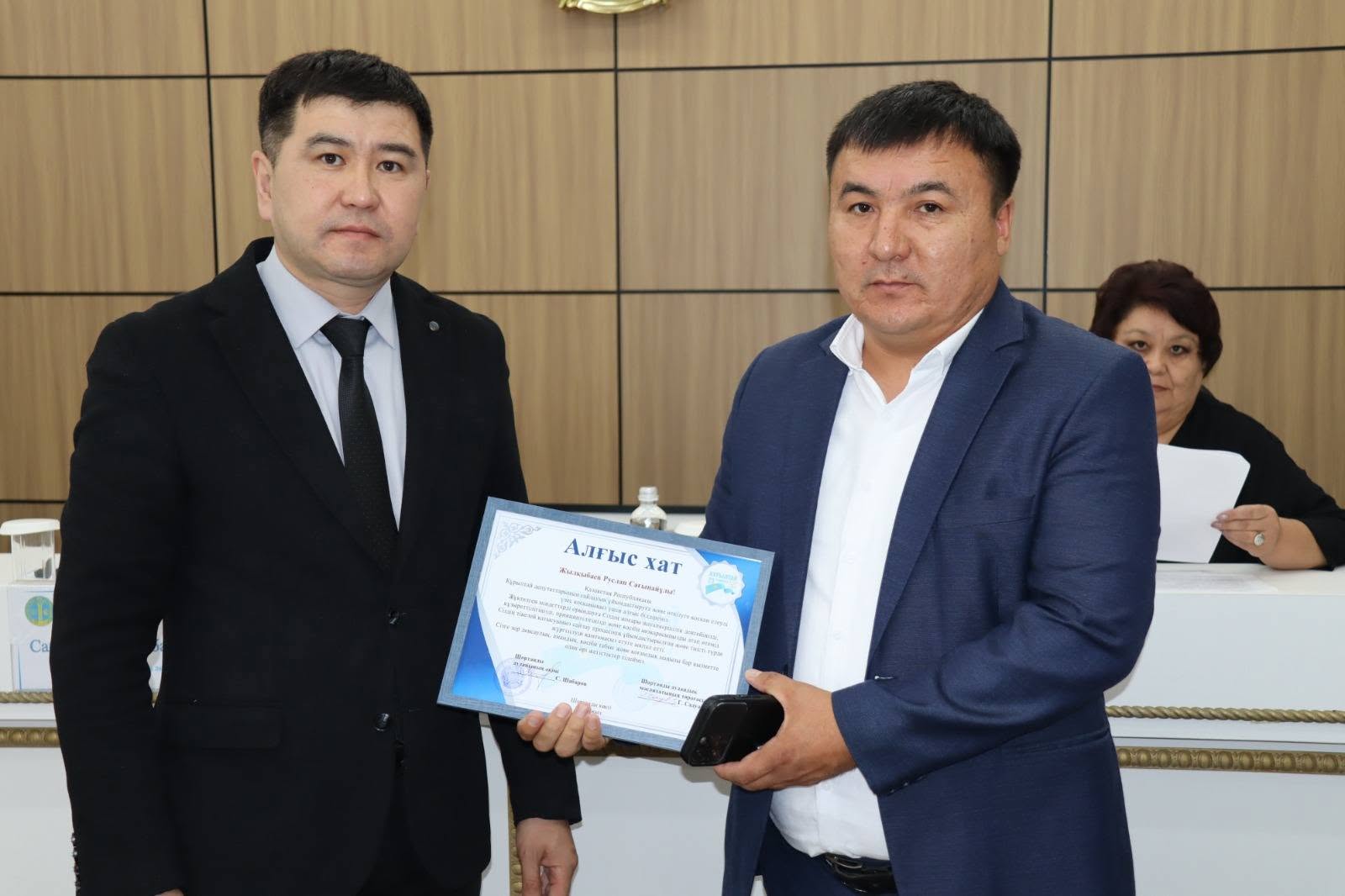 Екі ер адамның бірі екіншісіне «Алғыс хат» грамотасын табыстап жатқан сәті.