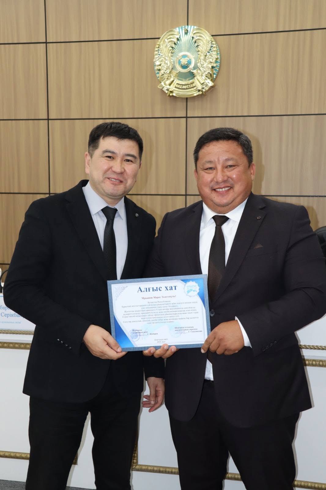 Екі ер адамның қолға алғыс хат ұстап тұрған суреті.