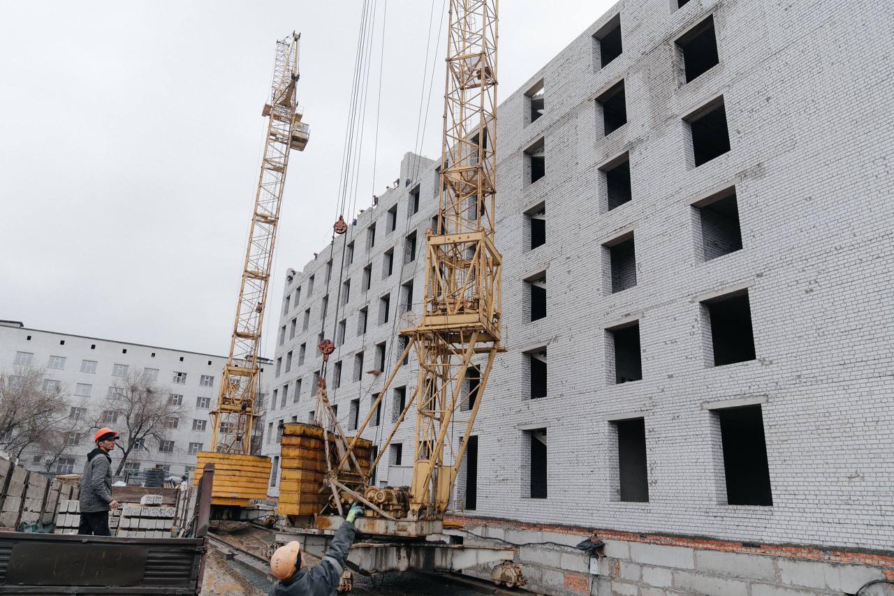 Құрылыс алаңындағы көпқабатты ғимарат және екі сары кран.