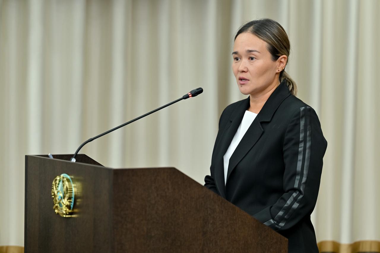 Трибунада сөйлеп тұрған қара костюмді әйел.