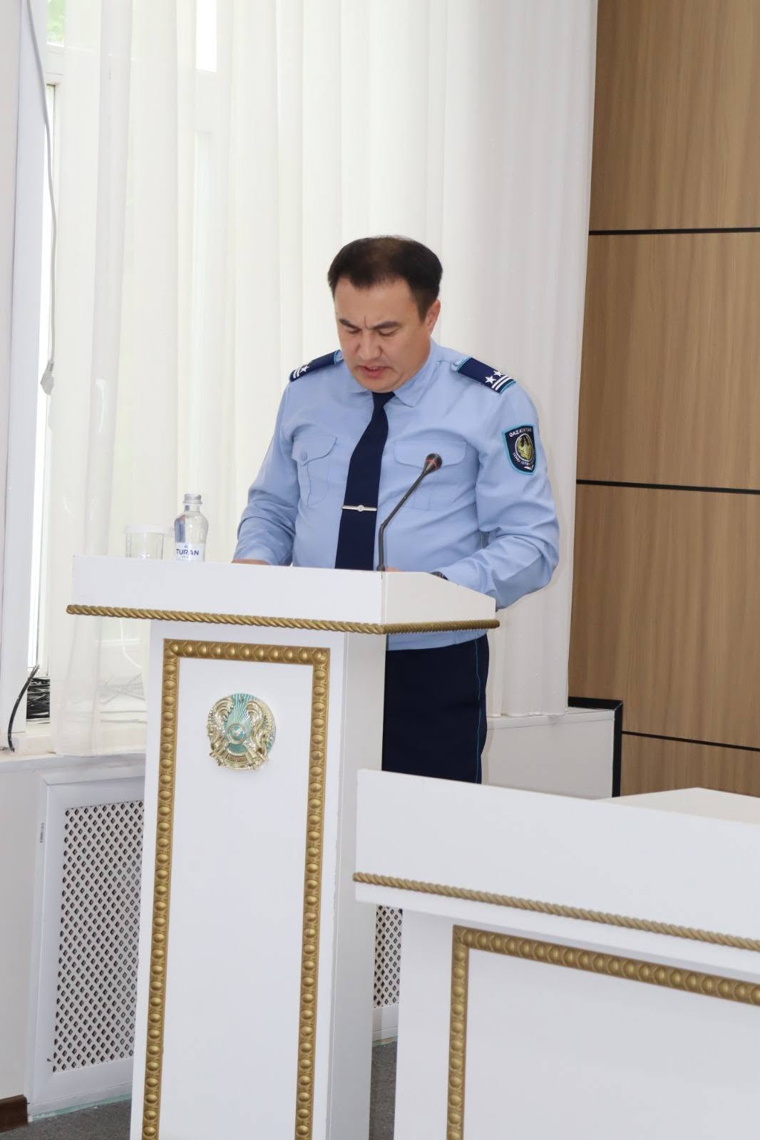 Форма киген ер адам трибунада сөйлеп тұр.