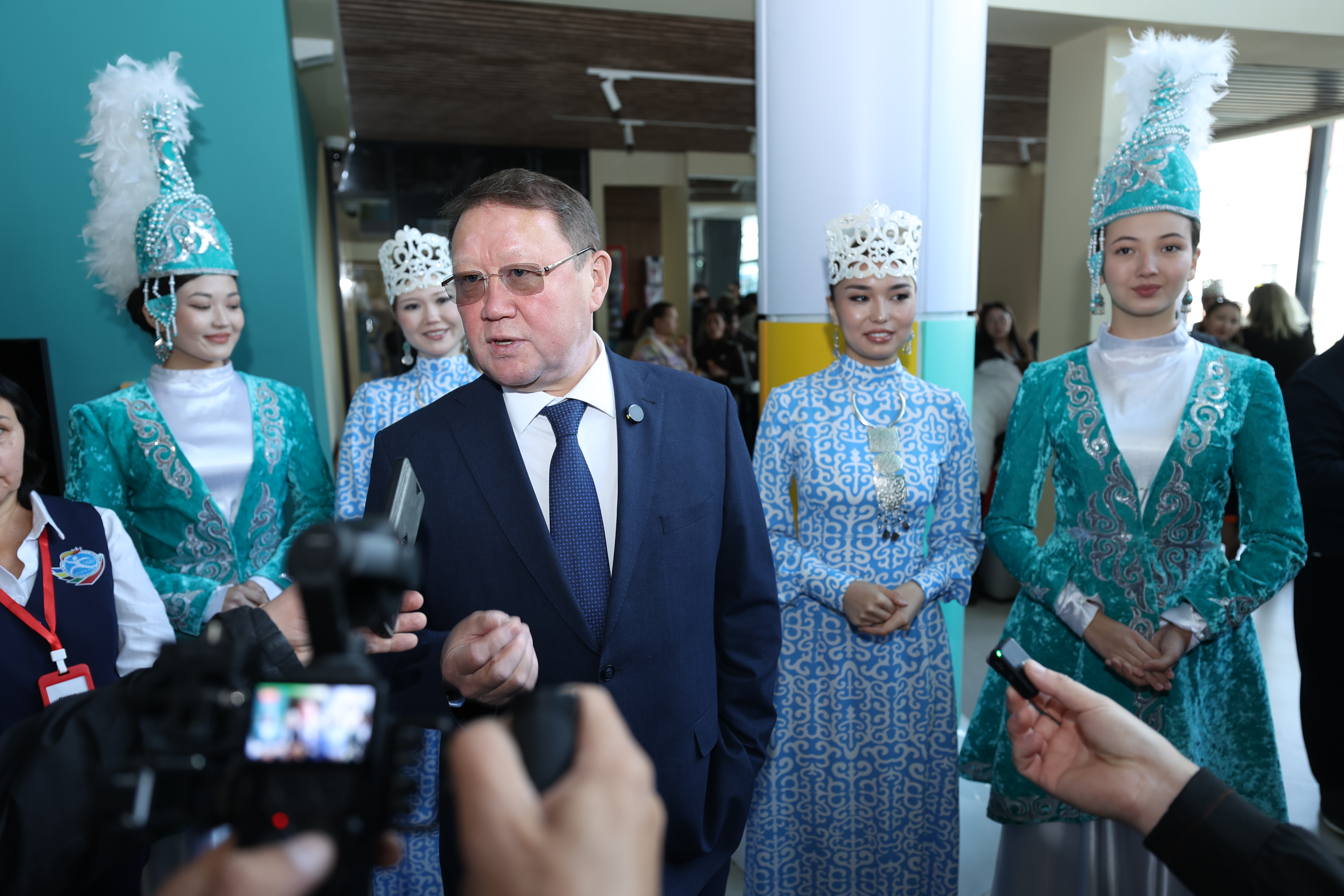 Облыс әкімі ұлттық киімдегі қыздар арасында журналистерге сұхбат беретін костюм киген.