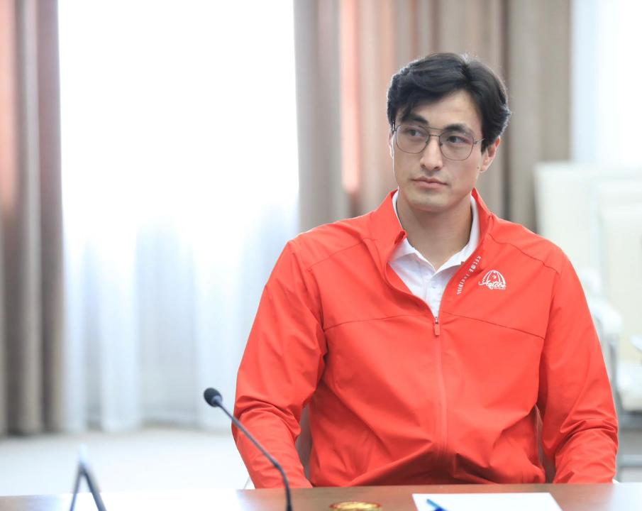Көзілдірік пен қызыл спорттық куртка киген ер адамның портреті.