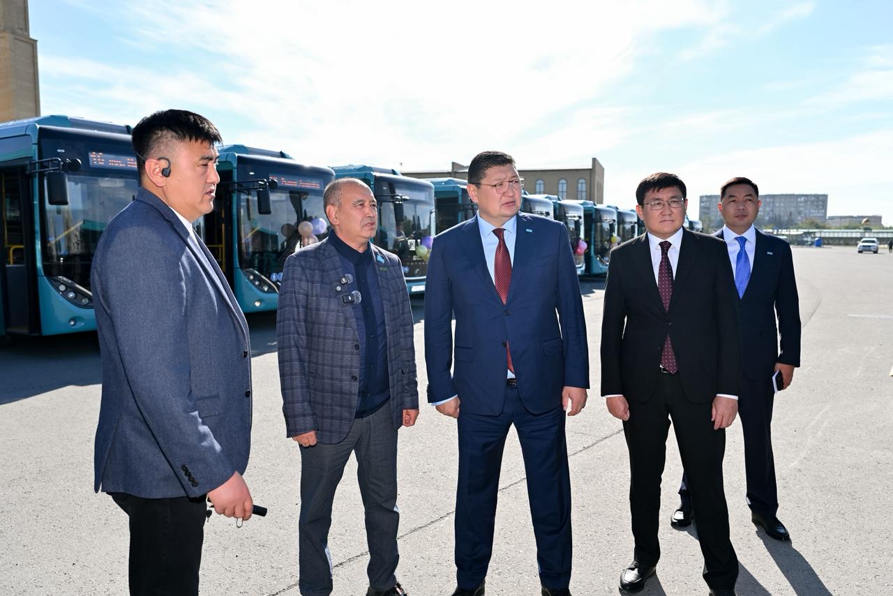 Көк түсті автобустардың алдында тұрған костюм киген ер адамдар тобы.