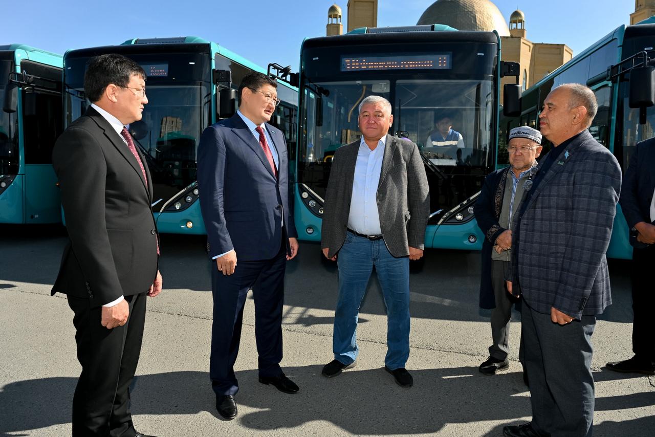 Көк түсті автобустардың алдында тұрған ер адамдар тобы.