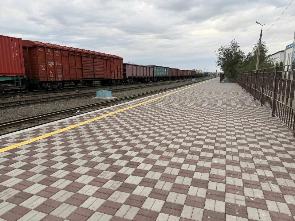 Теміржол бекетінің плиткалы алаңы және рельс бойында тұрған жүк вагондары.