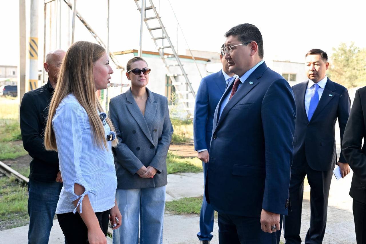 Көк костюм киген ер адамның әйелдер тобымен сыртқы алаңда сөйлесіп тұрғаны.