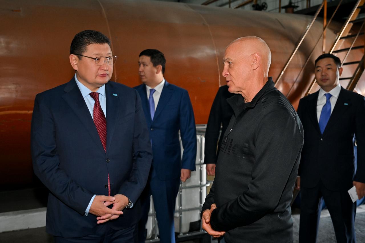Көк костюм киген ер адам мен қара киімді ер адамның өндіріс орнындағы сөйлесуі.