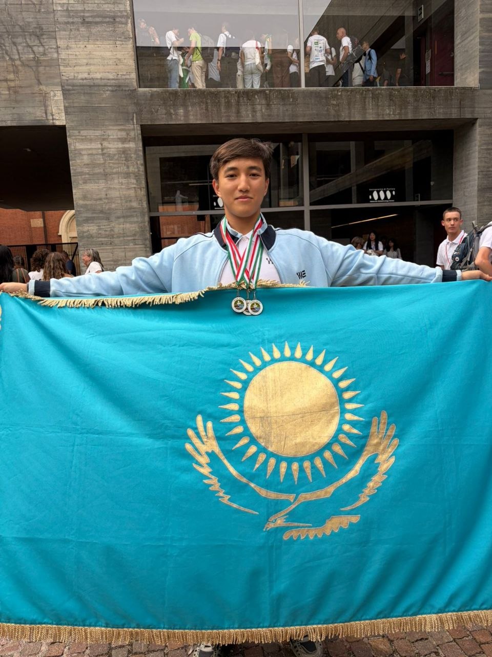 Спортсмен с медалями на шее держит в руках флаг Казахстана.