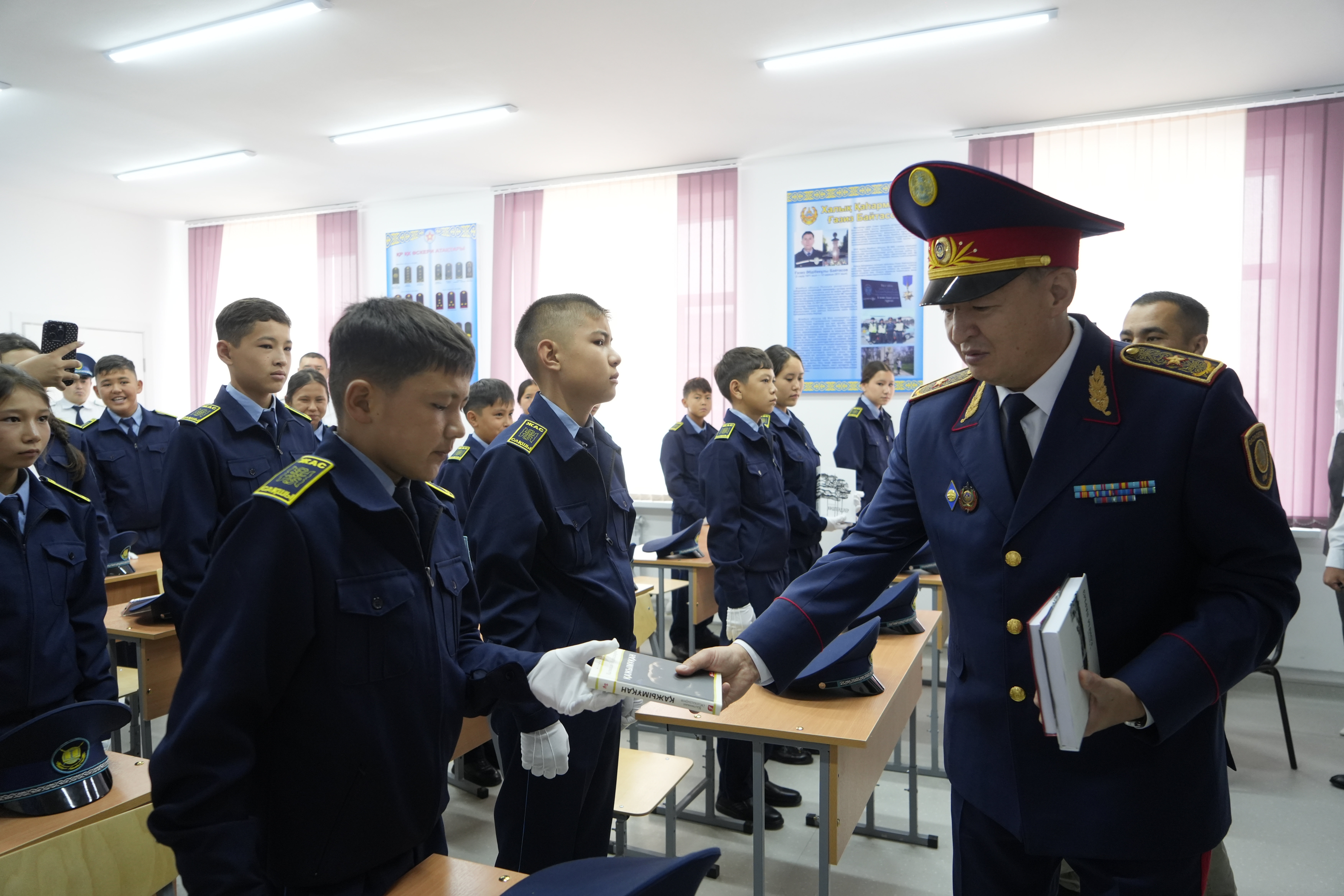 Форма киген офицер оқушыларға кітап табыстап жатыр.