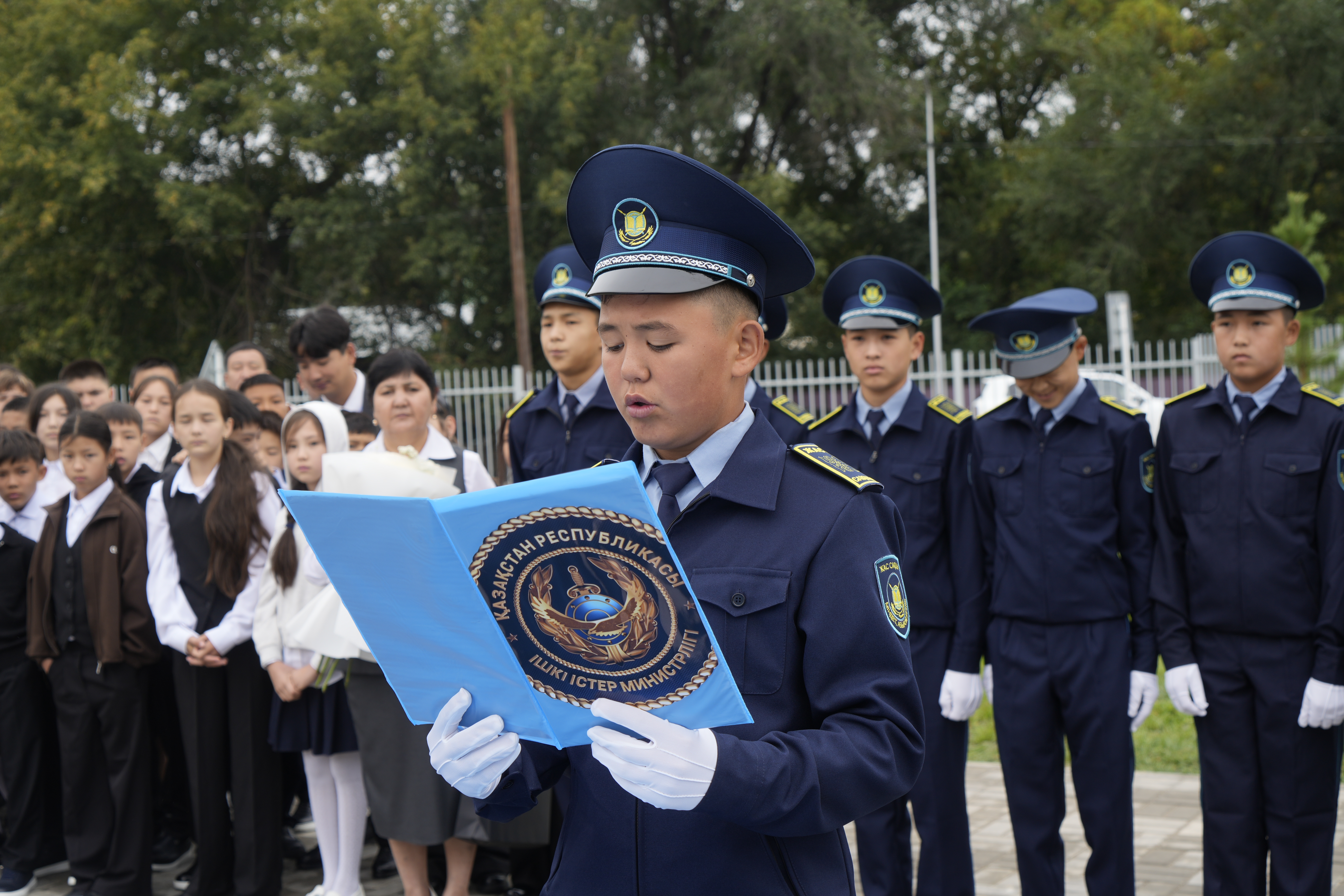 Форма киген жасөспірім Қазақстан Республикасы ІІМ эмблемасы бар көк папкадан мәтін оқып тұр.
