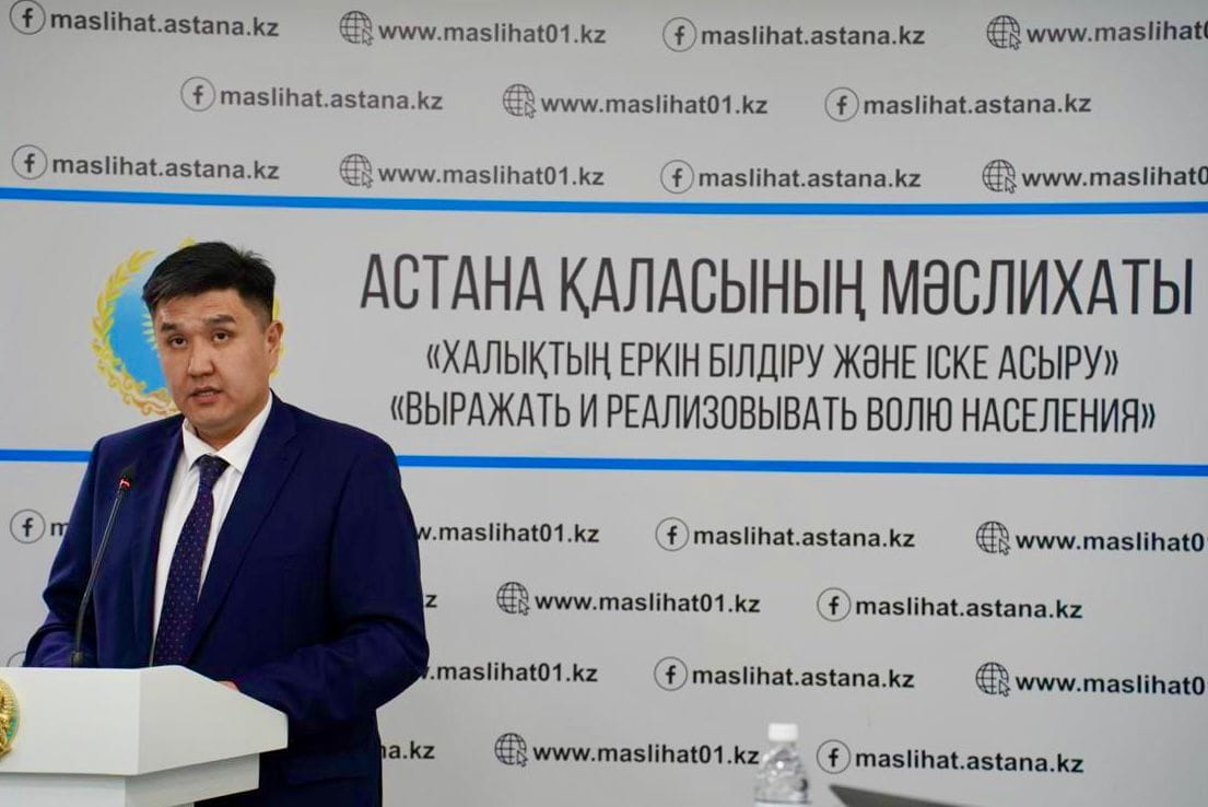 Астана қаласының мәслихатының фонында сөйлеп тұрған ер адам.