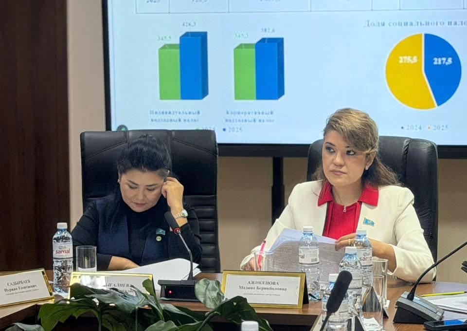 Экранда статистика көрсетілген жиналыста отырған екі әйел.