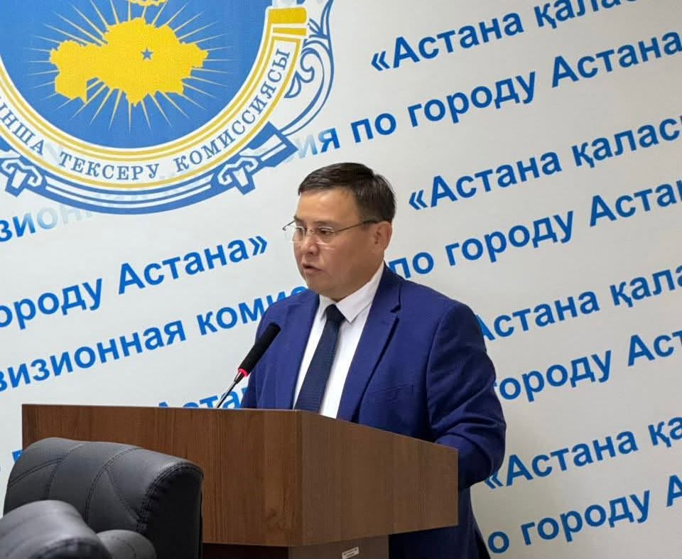Астана қаласының тексеру комиссиясының фонында трибунада сөйлеп тұрған ер адам.