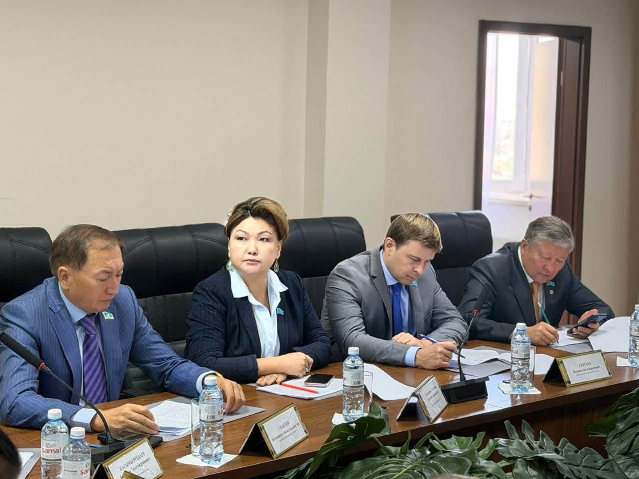 Жиналыс үстелінде отырған төрт ресми киінген адам.