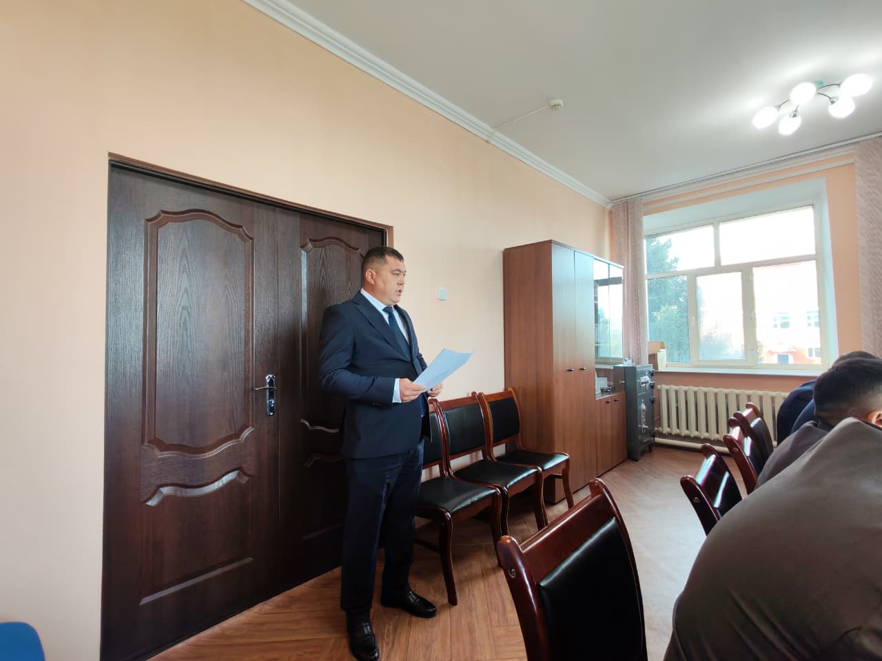 Костюм киген ер адам жиналыста қағаз оқып тұр.