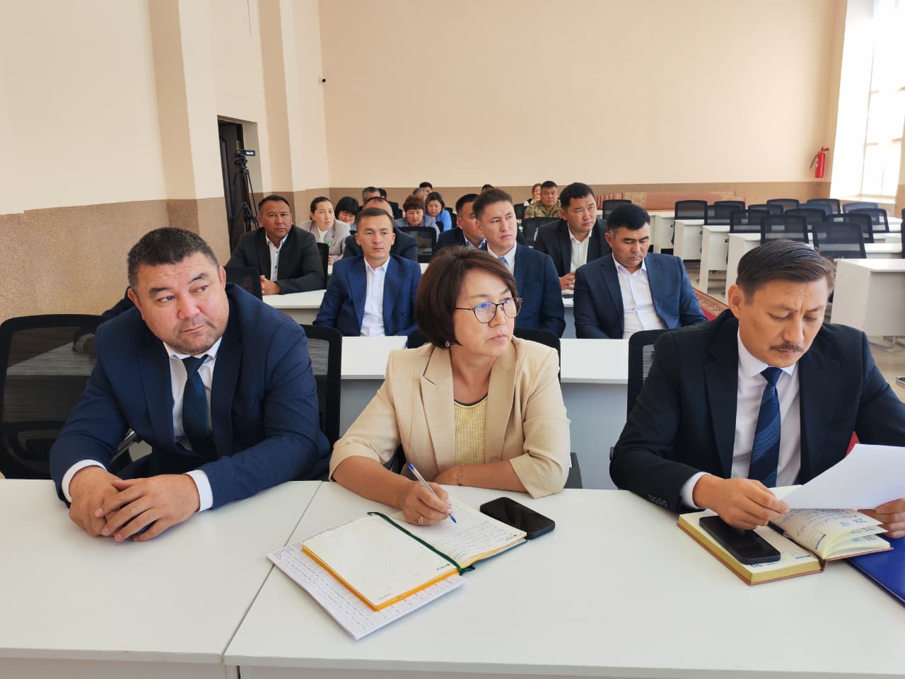 Сессияда отырған ресми киінген адамдар тобы.