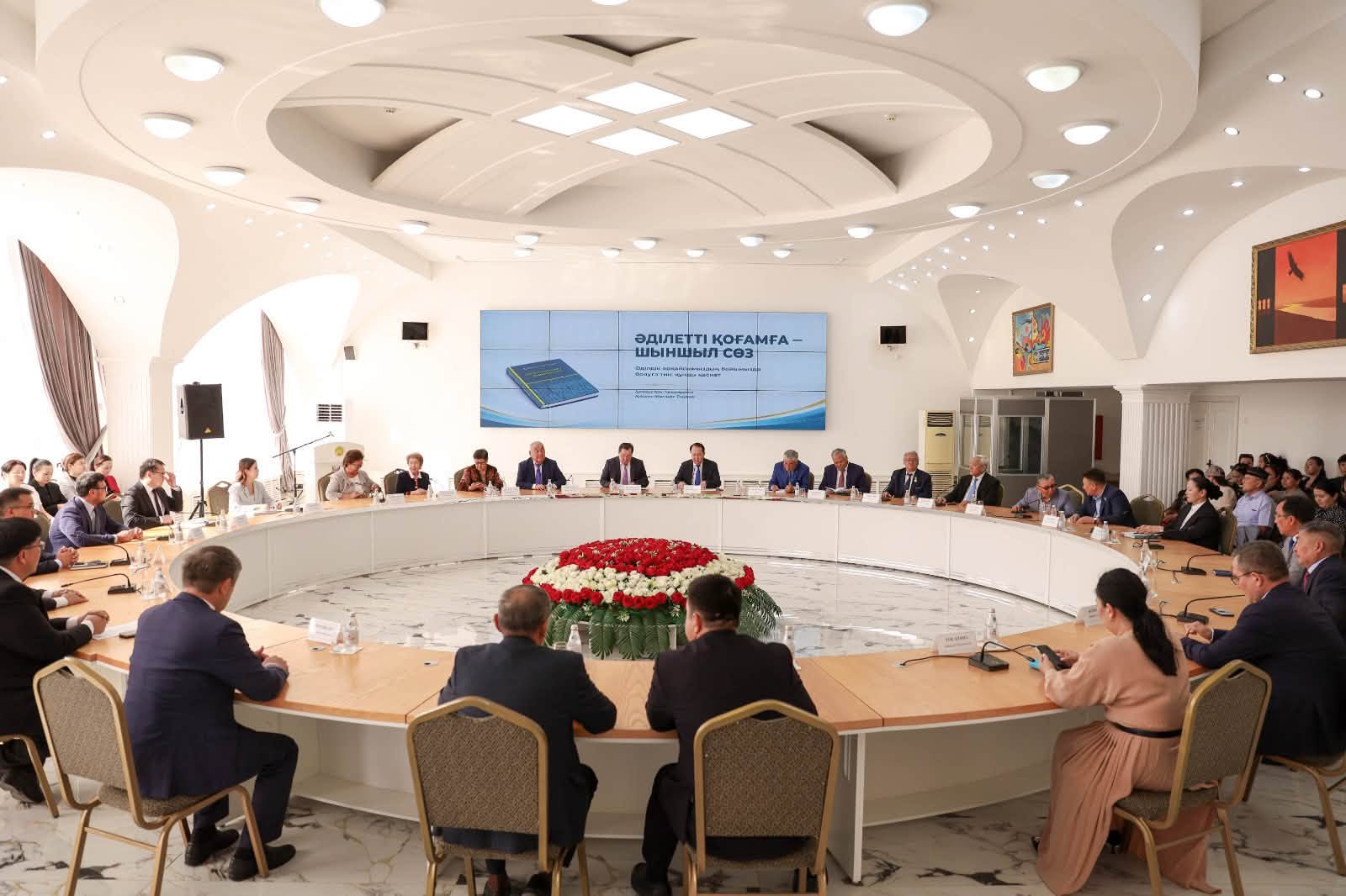 Дөңгелек үстелде жиналған адамдар және алдындағы «Әділетті қоғамға – шыншыл сөз» атты презентация экраны.