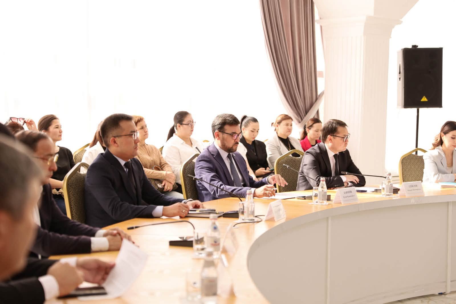 Конференцияда үстел басында отырған ресми киінген қатысушылар.