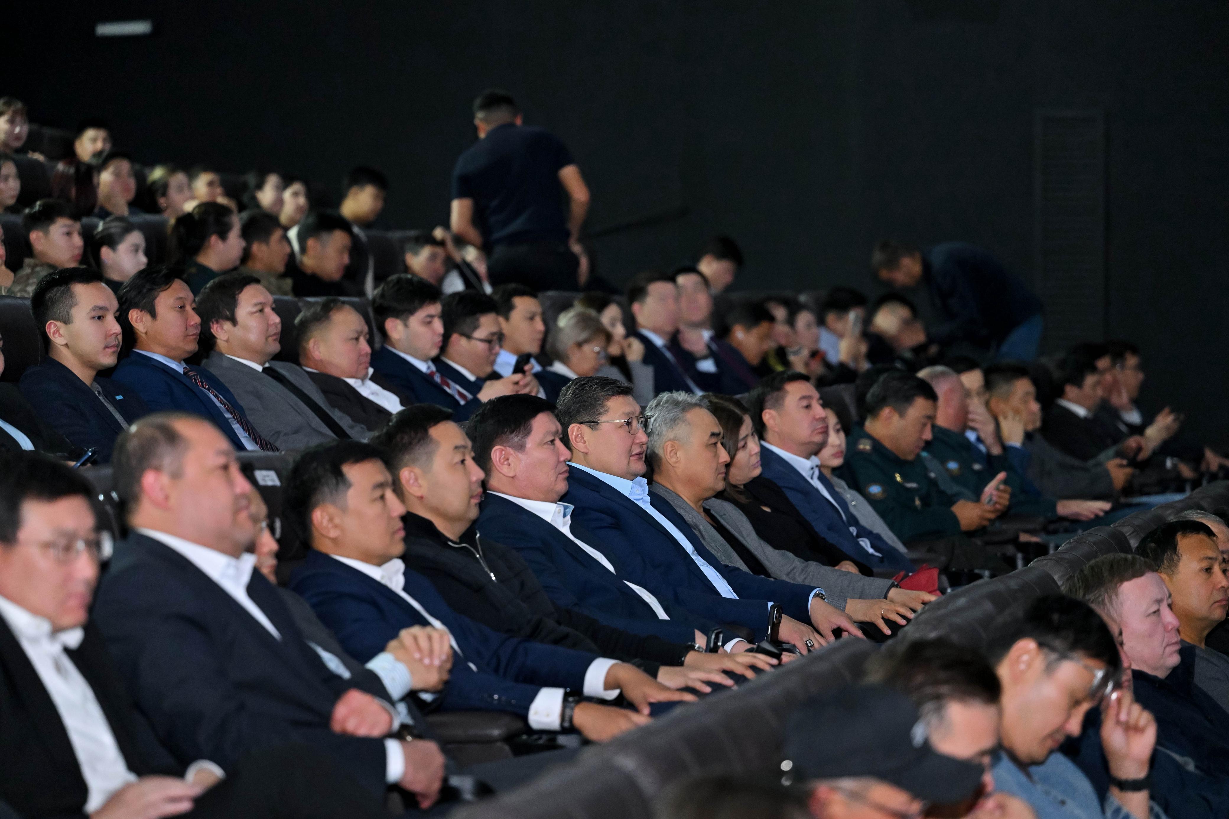 Костюм киген ер адамдардың жиналыста отырып, алға қарап тұрған топтық суреті.