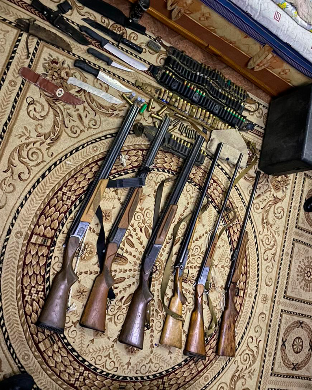 Кілемнің үстіне тізілген бірнеше мылтық, пышақтар және оқ-дәрілер.