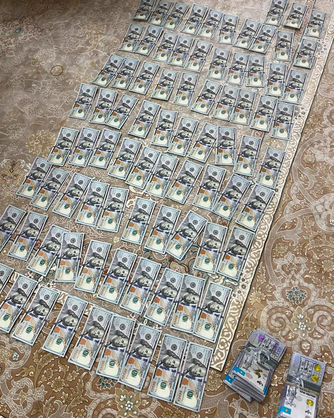 Кілемнің үстіне тізіліп жатқан көптеген 100 долларлық купюралар.