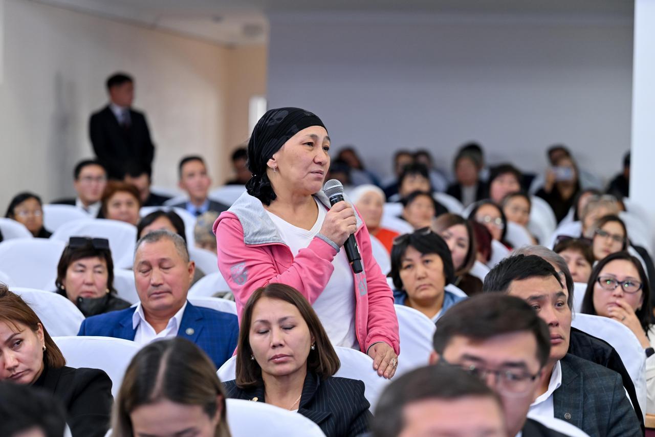 Конференцияда микрофон ұстап, сұрақ қойып жатқан әйел.