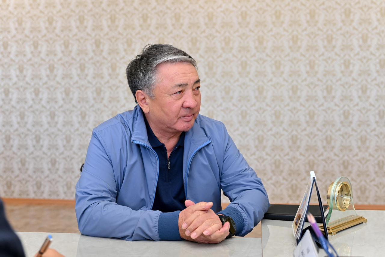 Көк түсті куртка киген, үстел басында отырған ер адамның портреті.