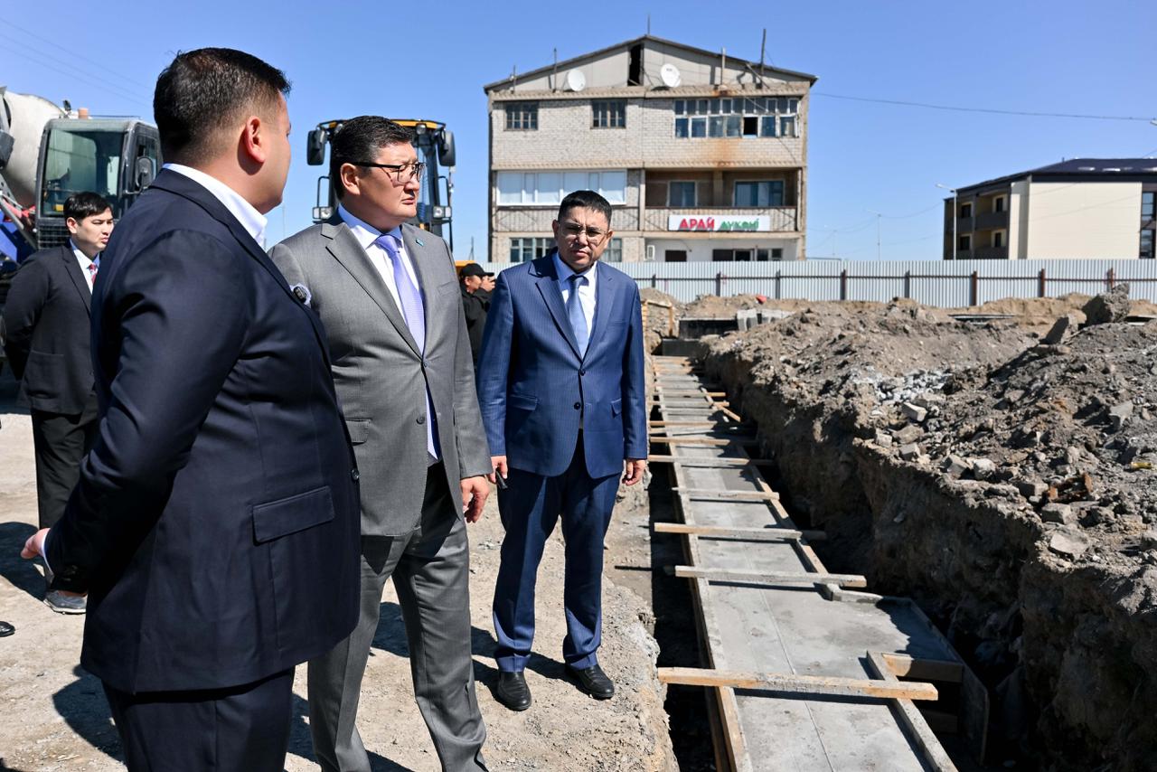 Костюм киген ер адамдар құрылыс алаңындағы жұмыстарды тексеріп жатыр.