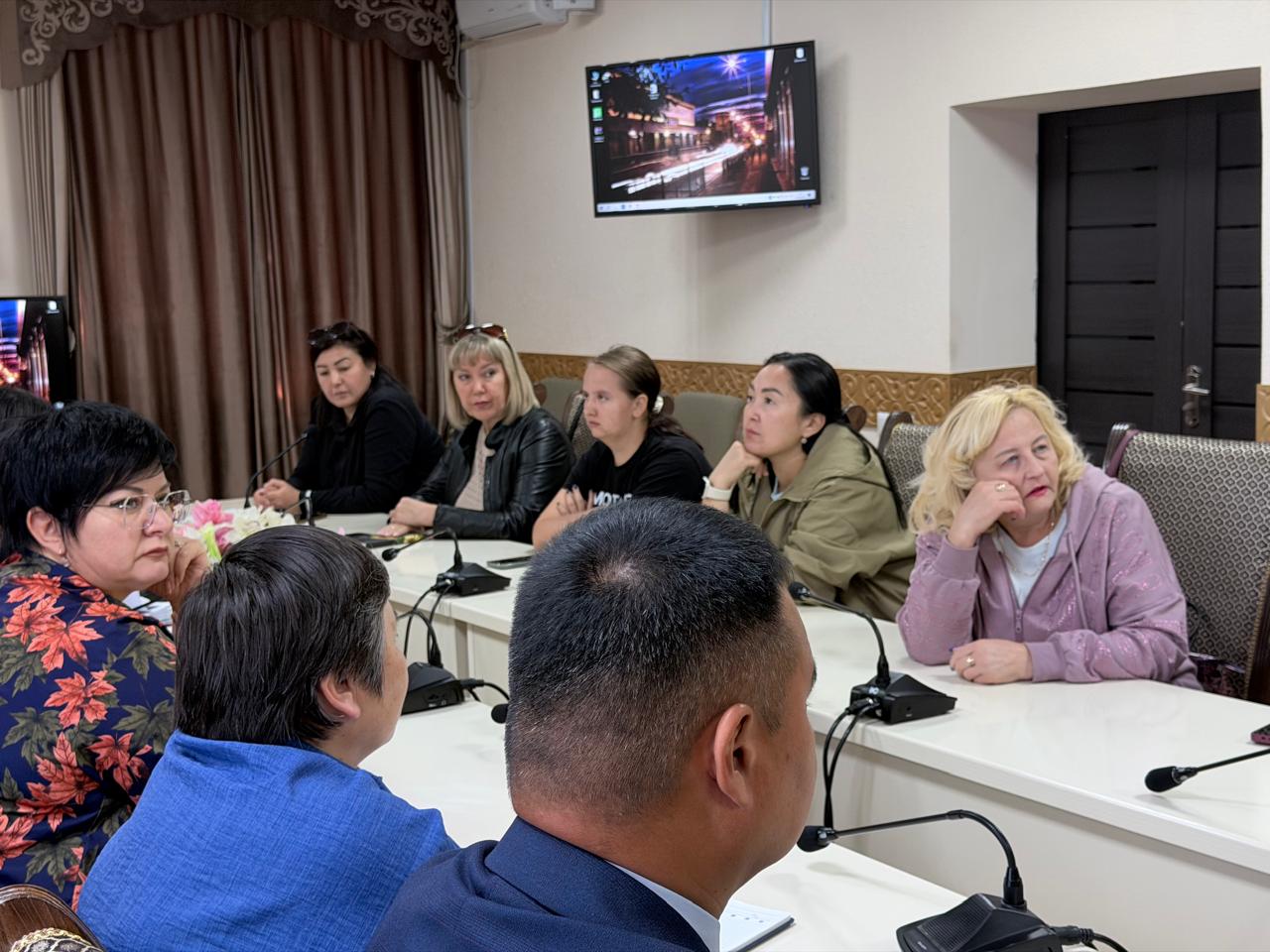 Келіссөз бөлмесіндегі үстел басында іскерлік кеңесте отырған адамдар тобы.